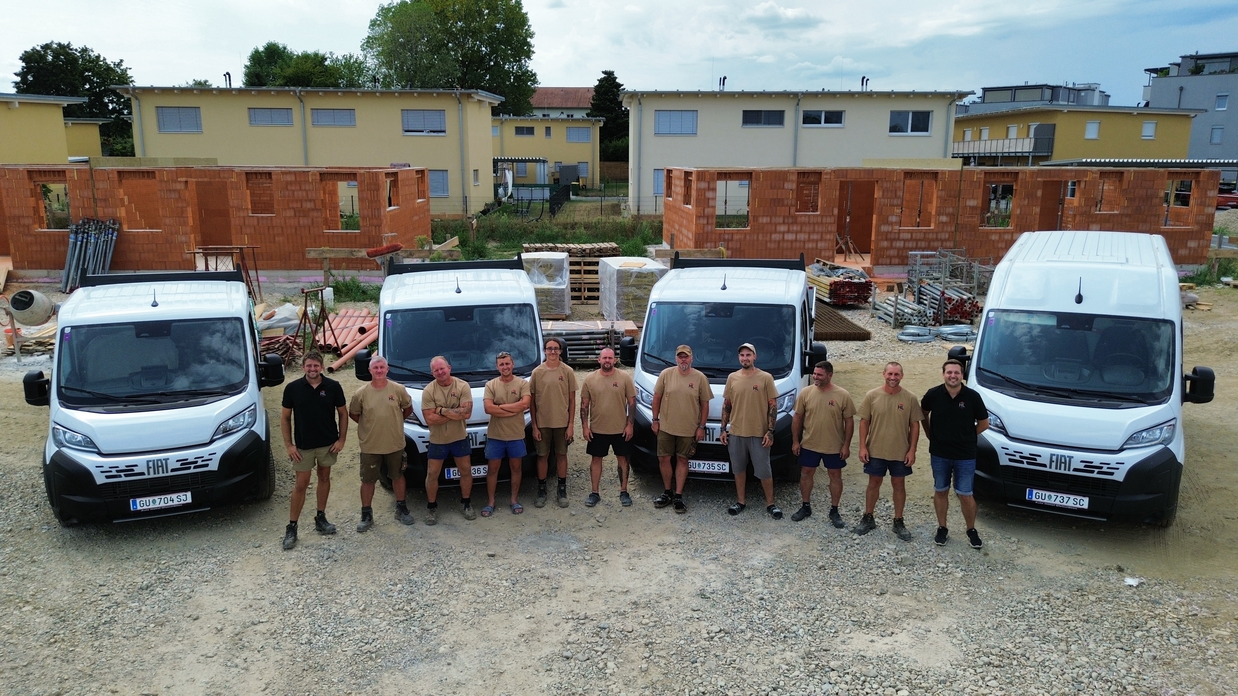 Team der HL Baumeister GmbH mit vier Fiat-Transportern vor Rohbauhäusern